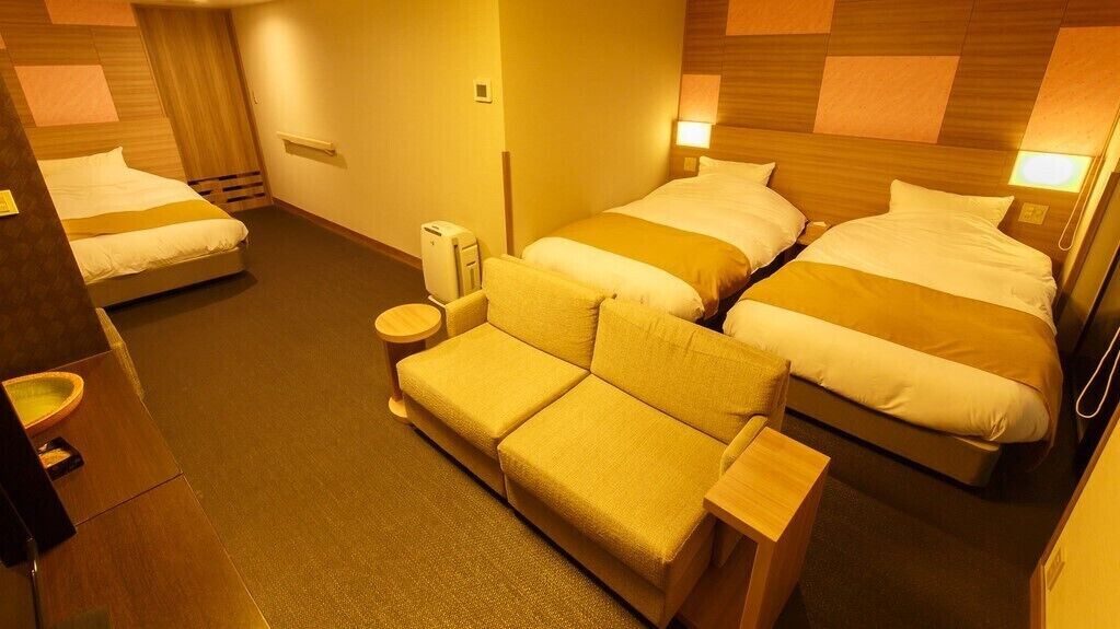Ein Hotelzimmer mit zwei Betten, einem Schlafsofa, einem Nachttisch, einer Lampe und einem Heizgerät.