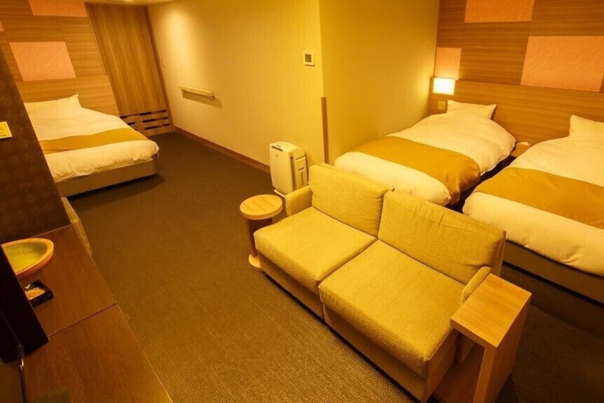 Ein Hotelzimmer mit zwei Betten, einem Schlafsofa, einem Nachttisch, einer Lampe und einem Heizgerät.