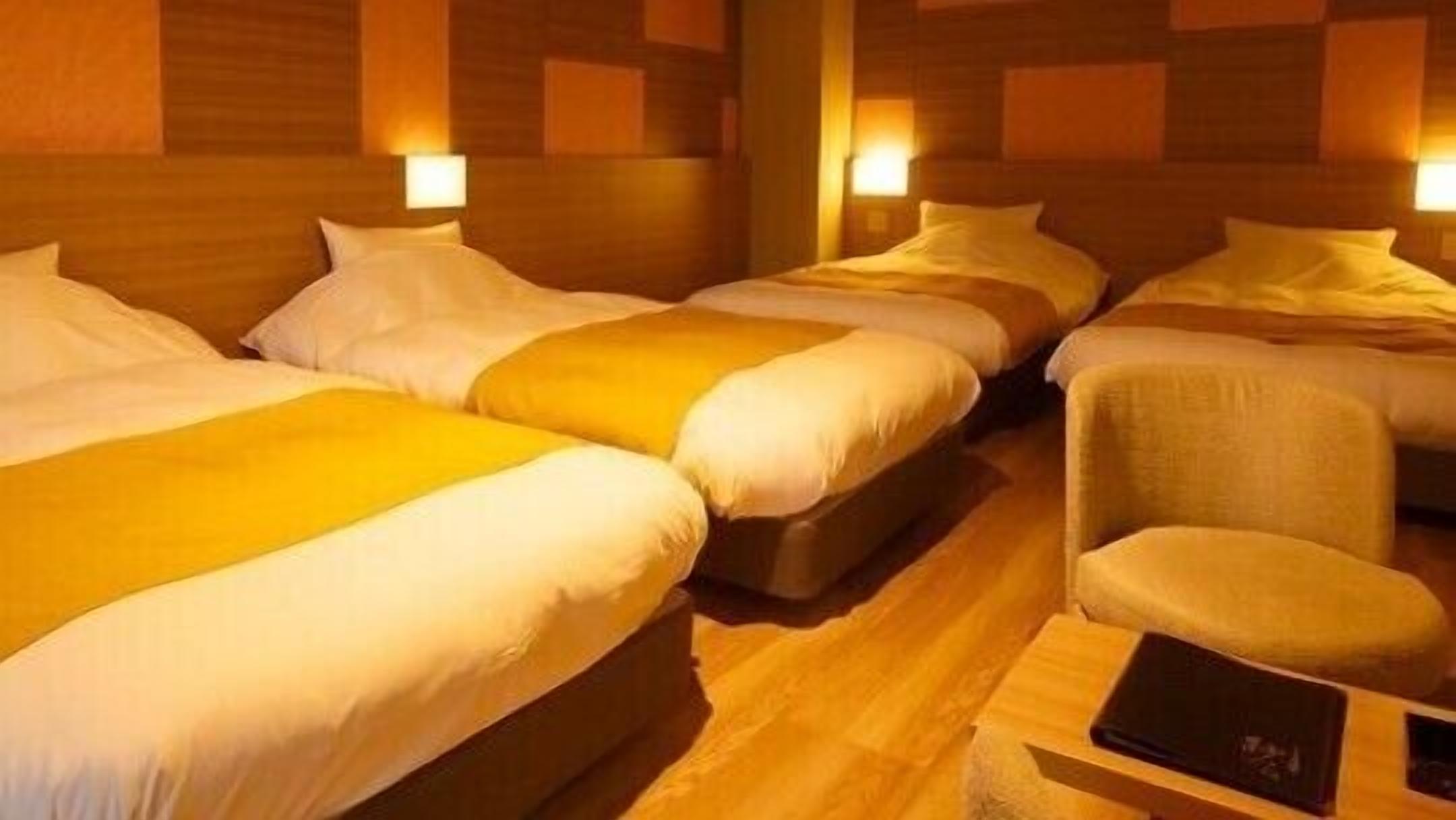 Ein Hotelzimmer mit drei Betten, Holzboden und Wandlampen.