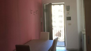A dining area with a table and chairs, a red wall, a ceiling with a light fixture, and a view of the outside through an open door. - Appartamenti Soperga (Milan)