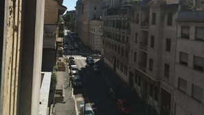 A narrow urban street lined with multi-story buildings, featuring parked cars and a clear blue sky. - Appartamenti Soperga (Milan)