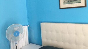 A room with a blue wall, a framed picture of a ship, a white headboard, and a standing fan. - Appartamenti Soperga (Milan)