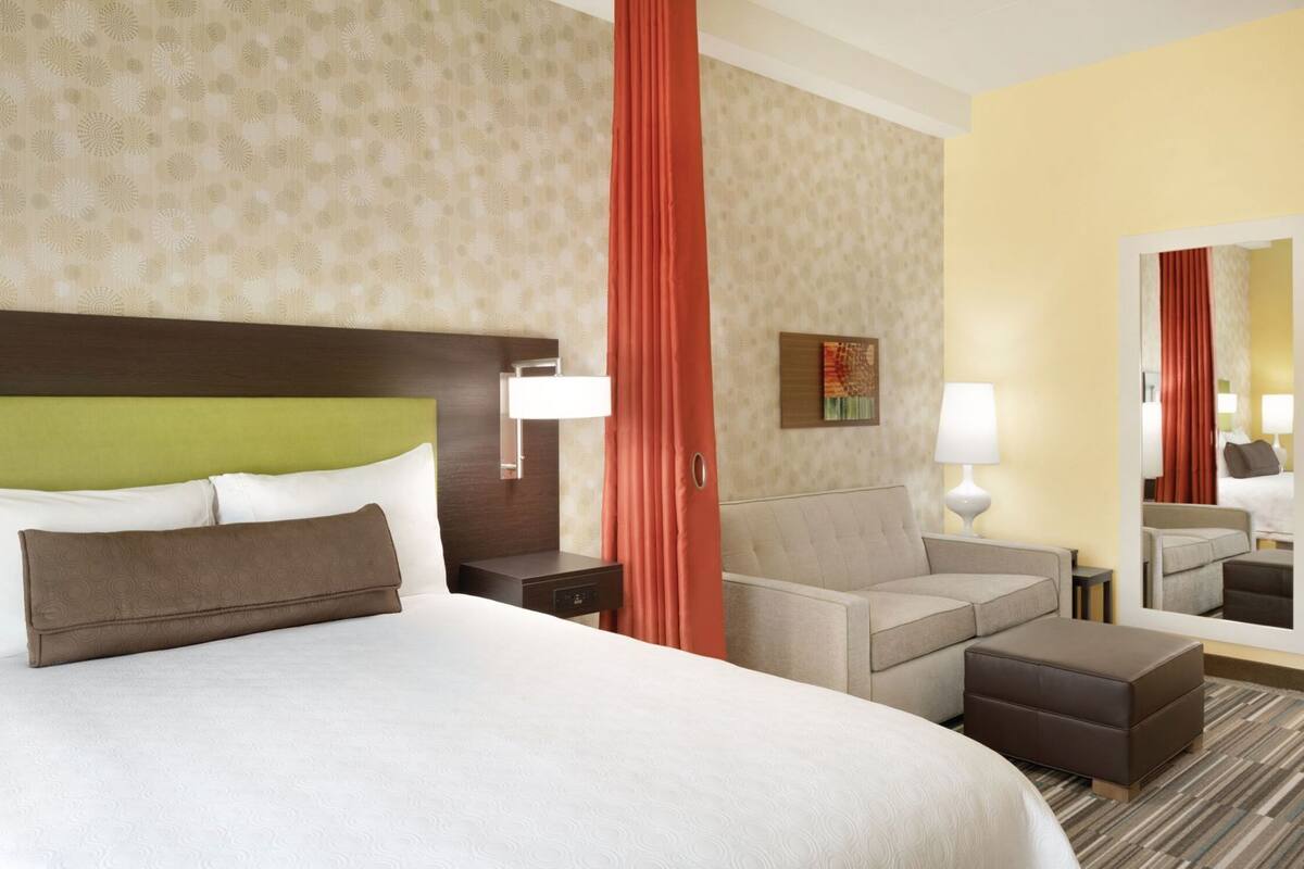 Een hotelkamer met een groot bed, een slaapbank, een klein tafeltje, een spiegel en een nachtkastje.