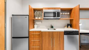 A compact kitchen with a refrigerator, microwave, dishwasher, wooden cabinets, and a countertop.