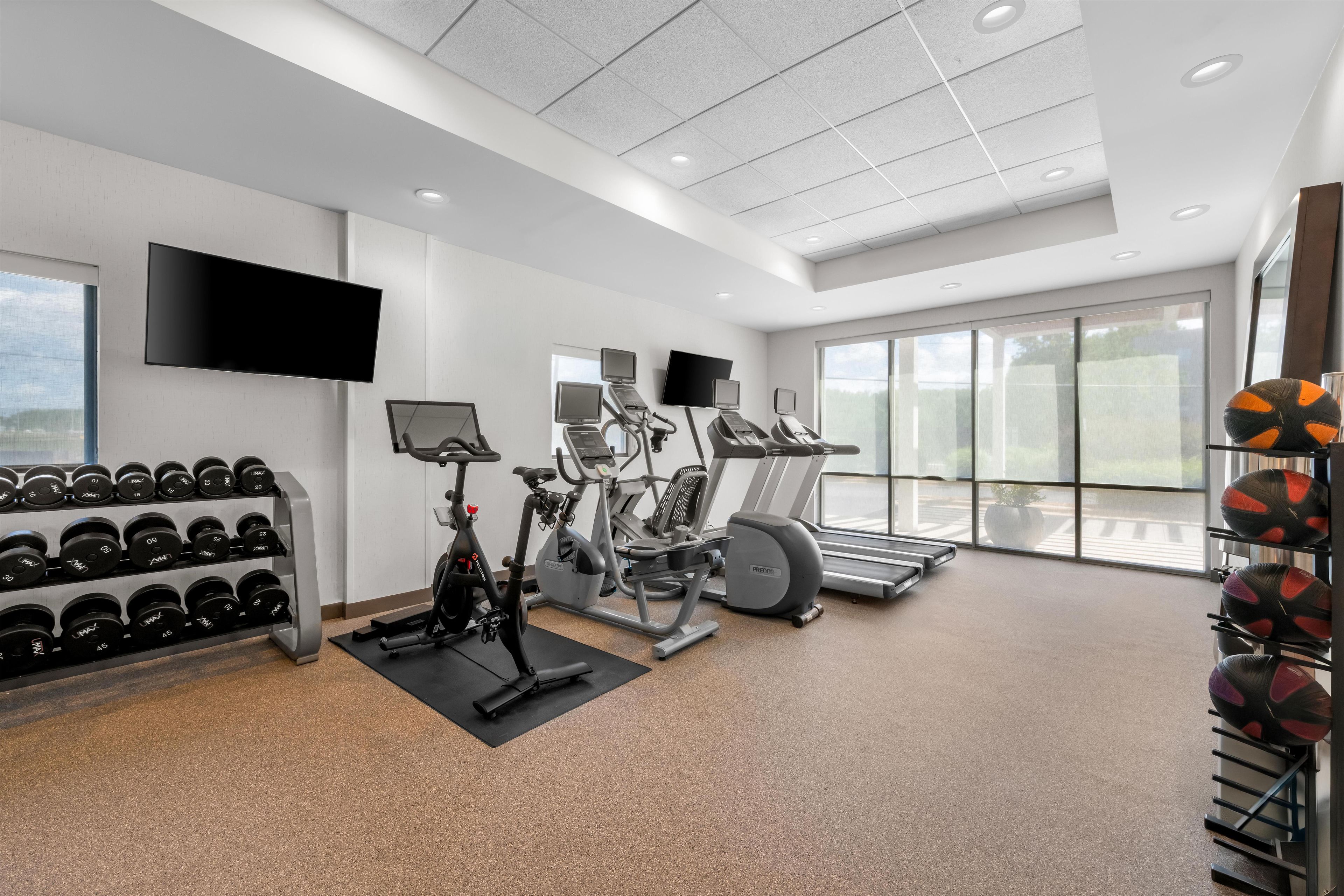 A gym with exercise equipment, a TV, and a rack of dumbbells.