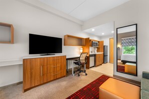 Een moderne hotelkamer met een flatscreen televisie, houten kasten, een kitchenette, een bureau en een grote spiegel.