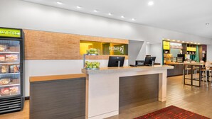 Zona de recepción de un hotel con mostrador, refrigerador y área de descanso.