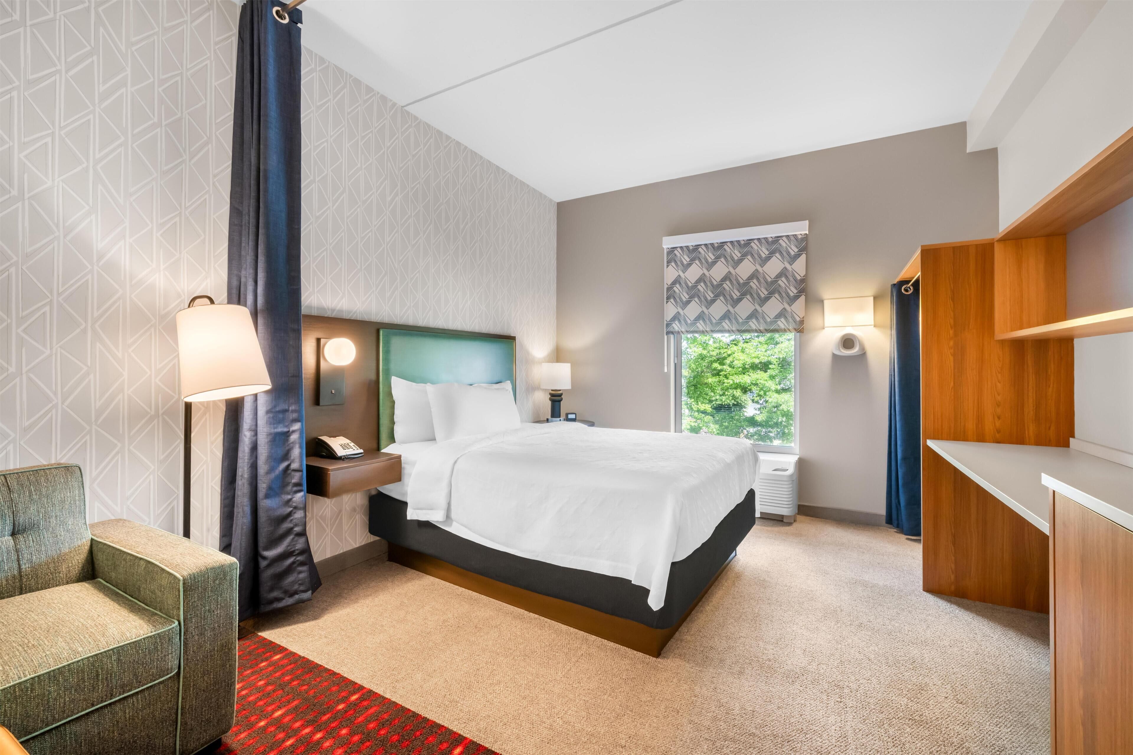Habitación de hotel con cama, mesitas de noche, escritorio, una silla y ventana con vistas a zonas verdes.
