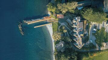 An aerial view of a coastal property with a dock, a large house with a sloped roof, and surrounding greenery.