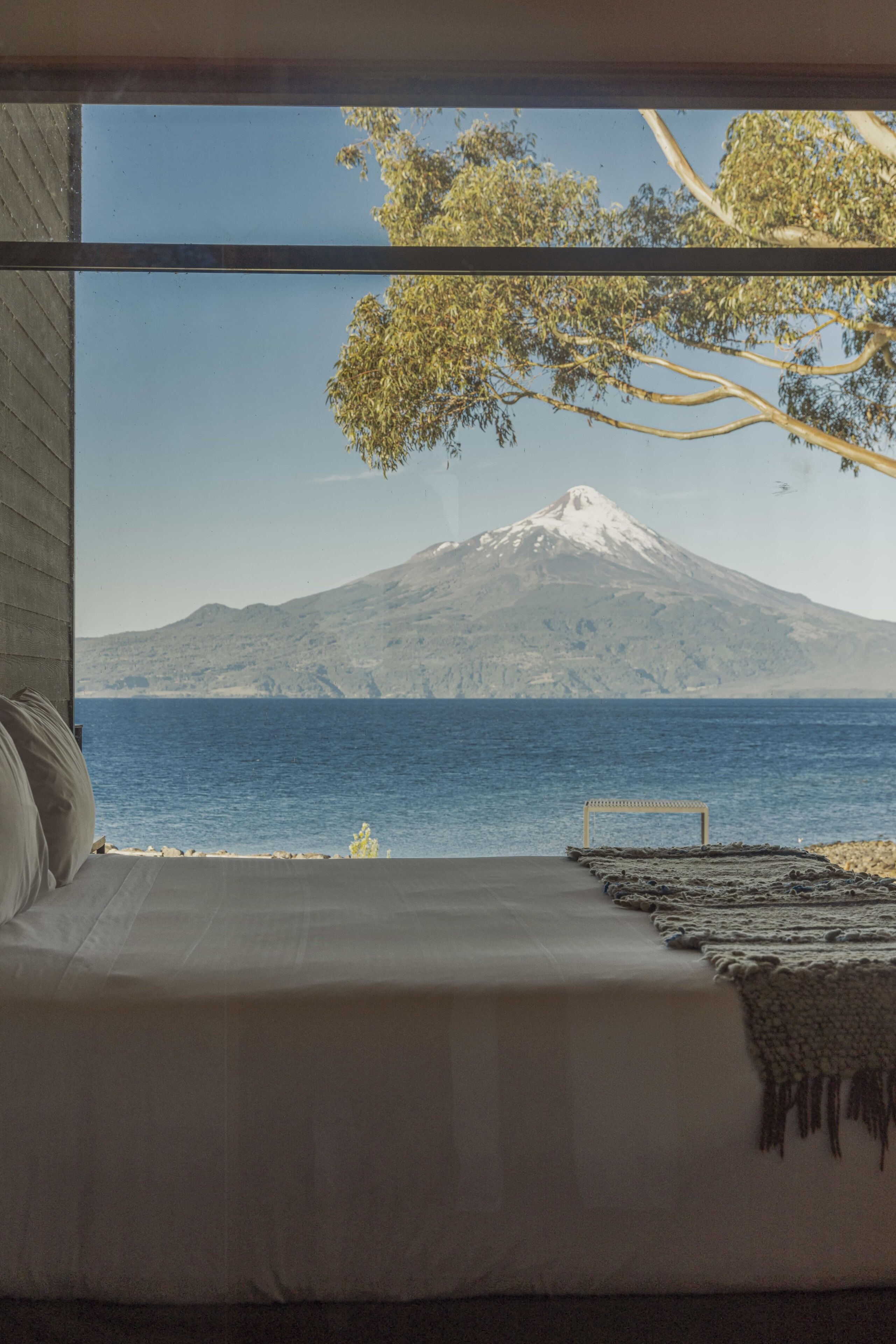 A bed with a view of a mountain and a body of water.