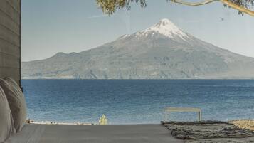 A bed with a view of a mountain and a body of water.