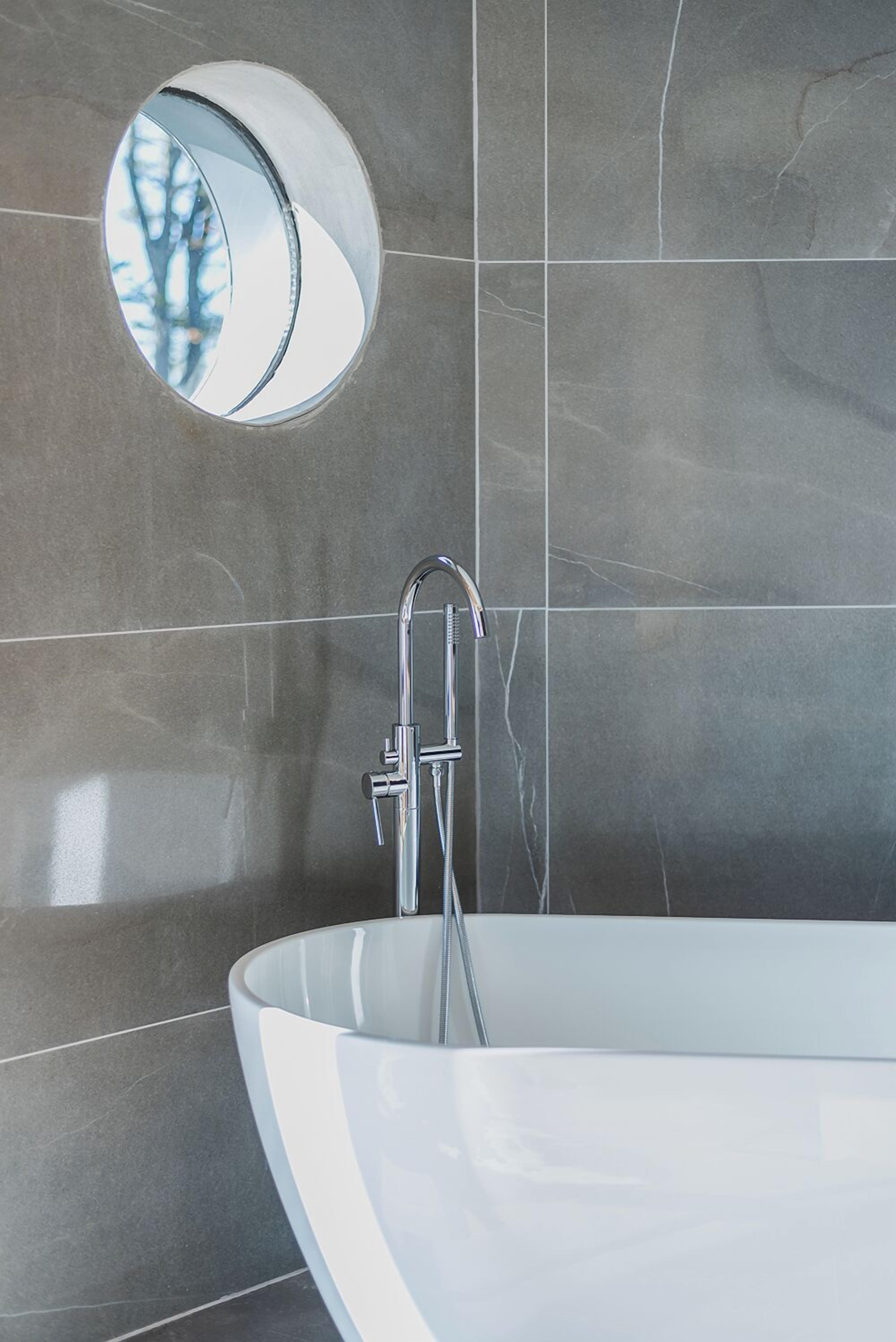 A modern bathroom with a freestanding bathtub, a round mirror, and a chrome faucet.