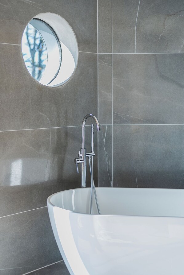 Une salle de bain moderne avec une baignoire sur pieds, un miroir rond et un robinet chromé.