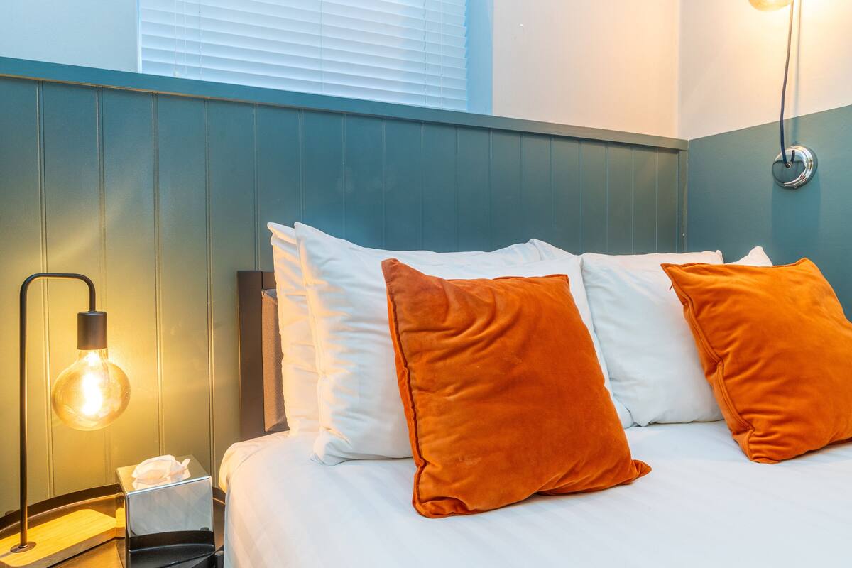 A neatly made bed with white and orange pillows, a bedside lamp, and a tissue box.
