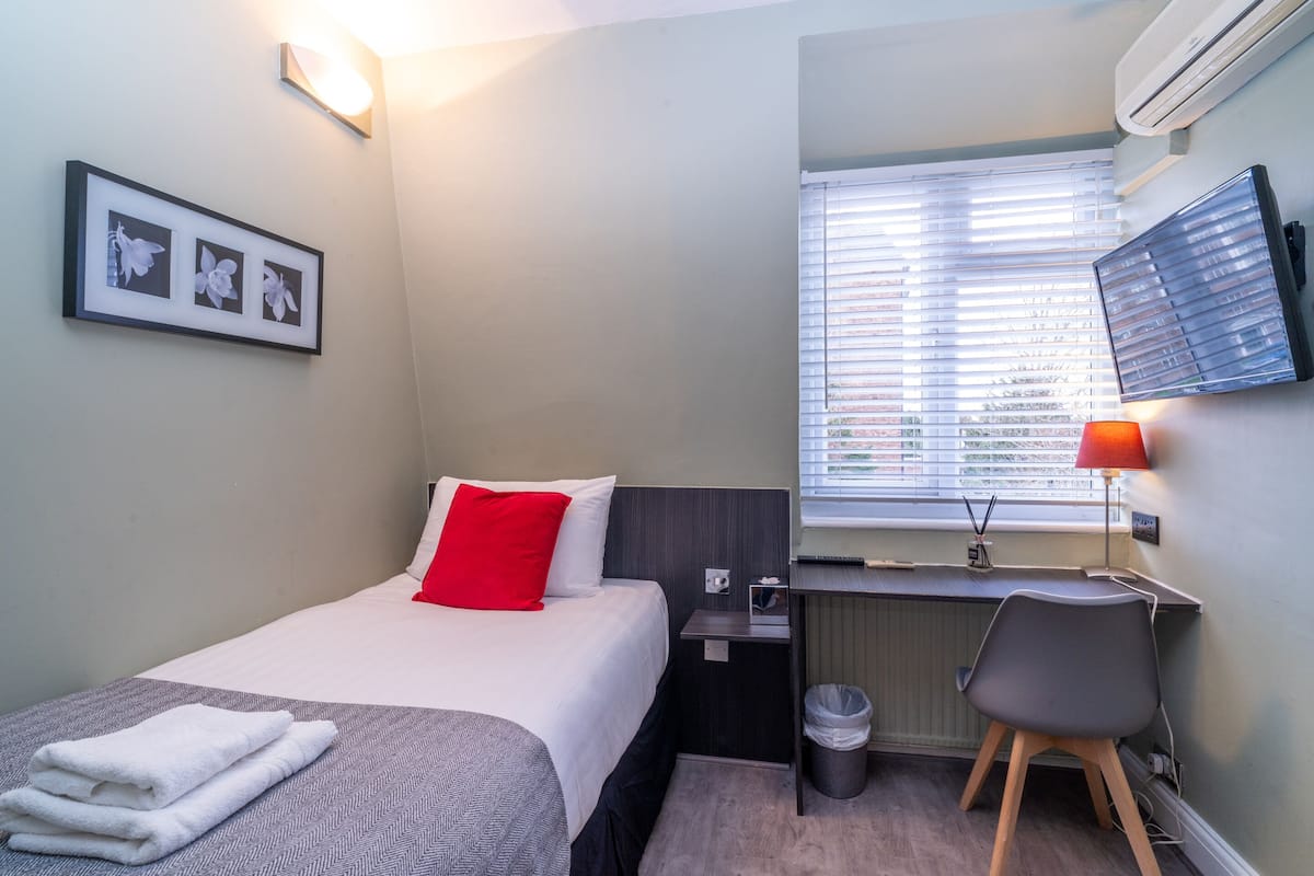 A hotel room with a bed, a desk, a chair, a TV, and a window with blinds.