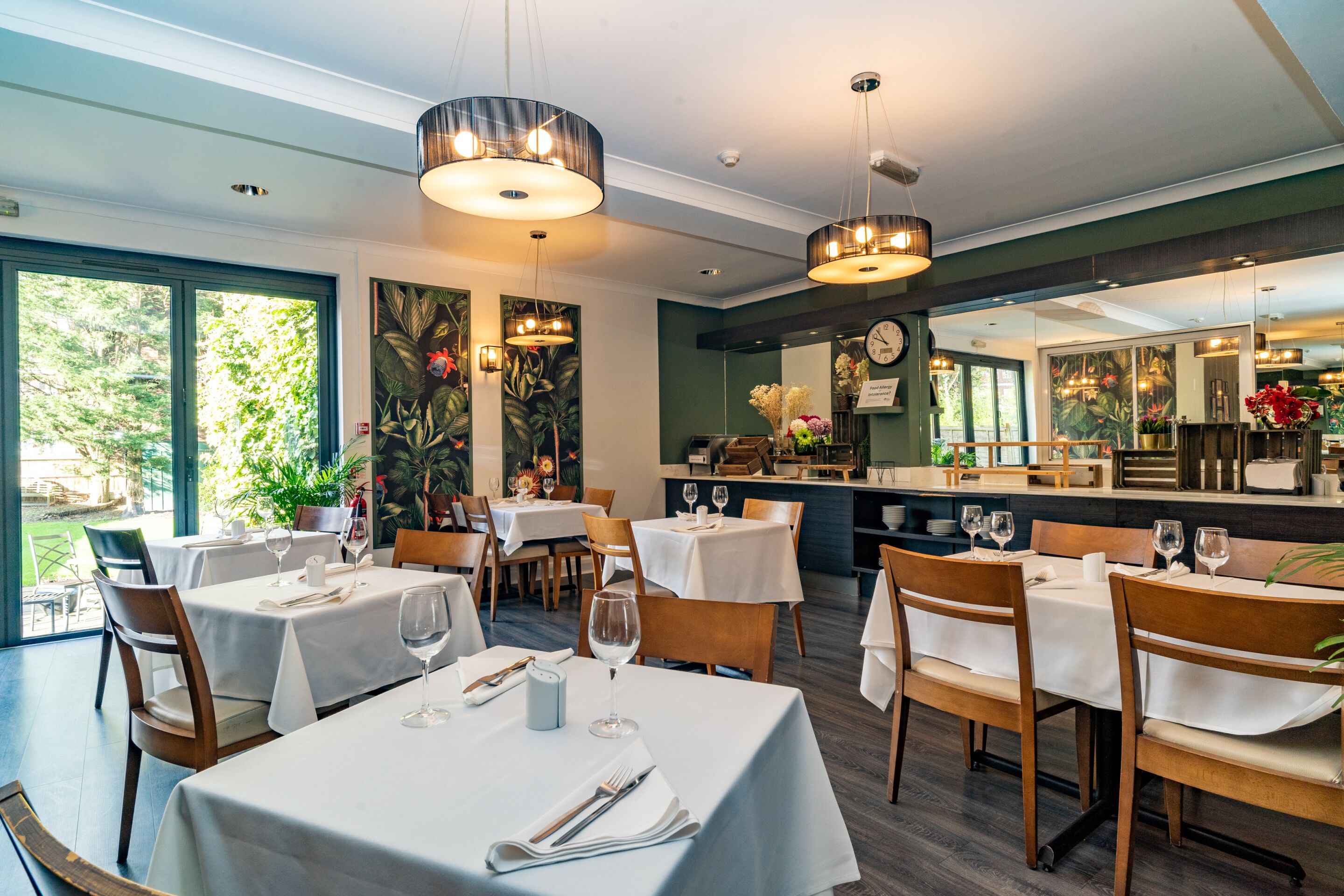 A restaurant with tables set for dining, large windows, and hanging light fixtures.