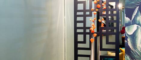 A room with a decorative black partition, a metal stand with orange flowers, and a colorful wall with a leaf pattern.