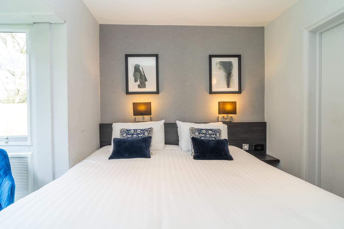 A modern hotel room with a large bed, two wall-mounted lamps, and framed artwork above the bed.