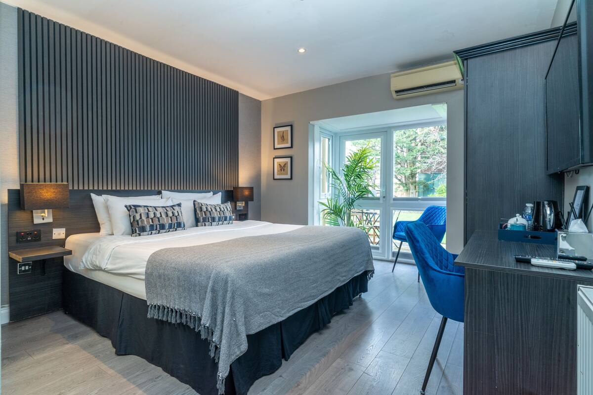A modern bedroom with a large bed, bedside tables, a desk, and a view of the outdoors.