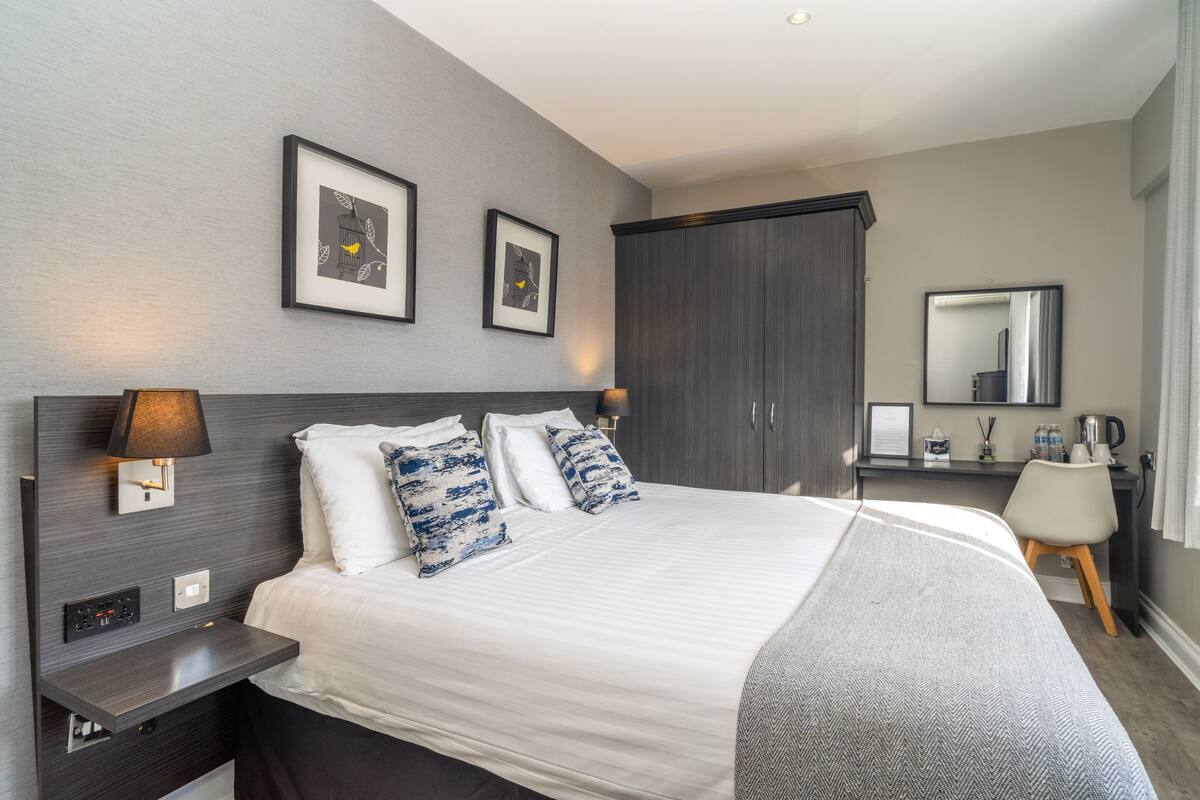 A modern hotel room with a large bed, a desk, a wardrobe, and a mirror.