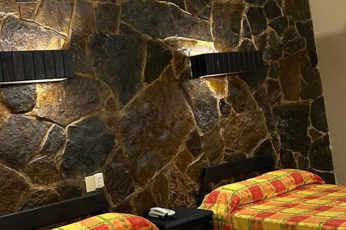 Une chambre d’hôtel avec un mur en pierre, deux lits avec une literie aux couleurs vives et une petite table avec un téléphone.