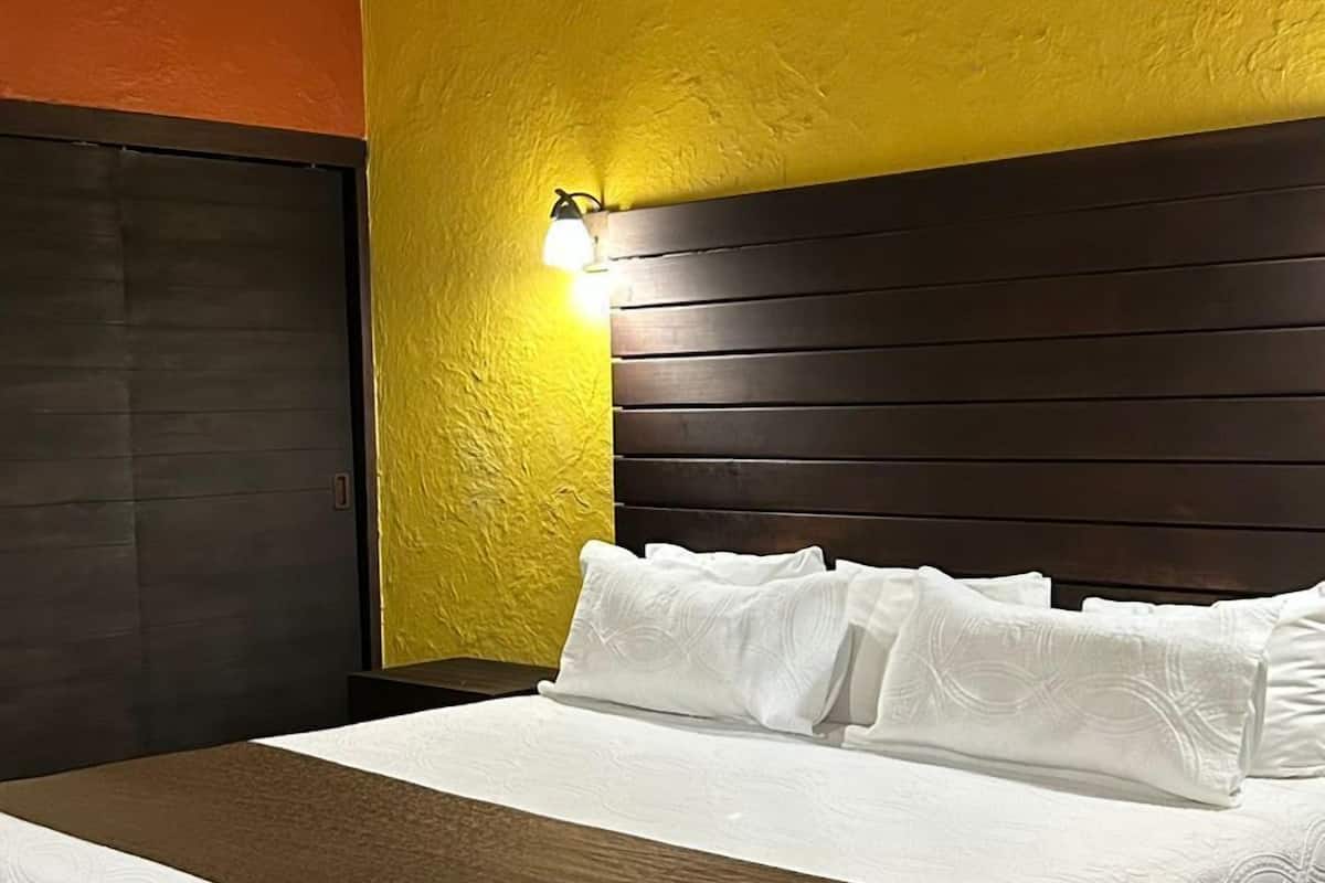 Un lit avec une couvre-lit blanche et des oreillers, une tête de lit en bois et un mur aux couleurs jaune et orange.