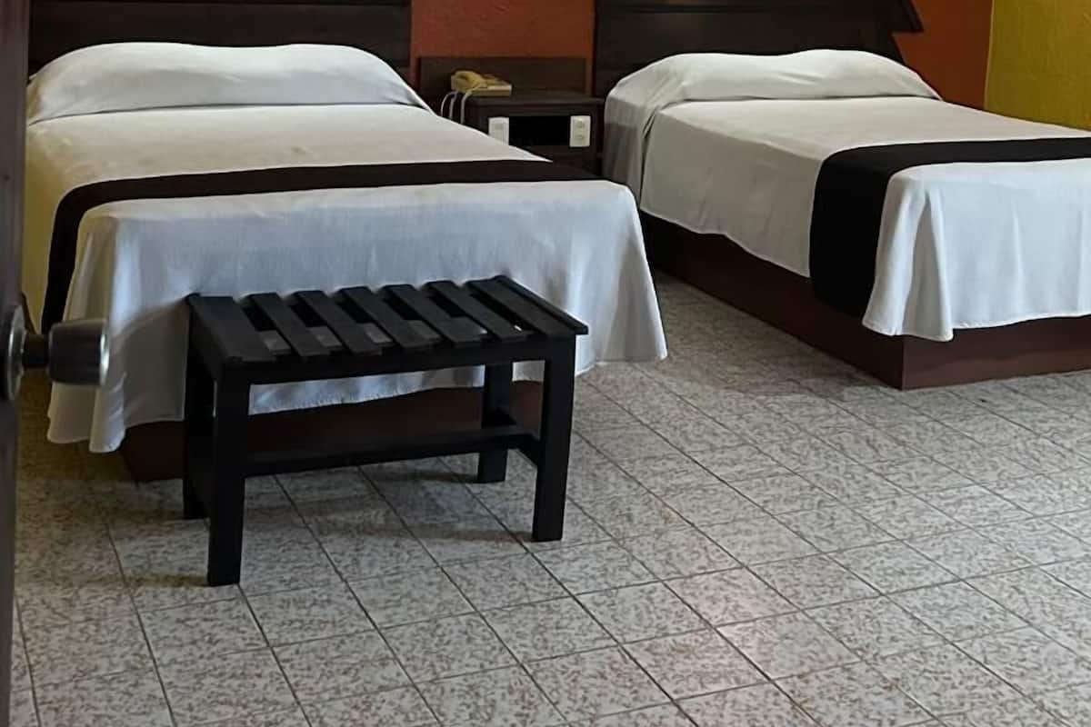 Une chambre d’hôtel avec deux lits, une banquette, une table de chevet et un luminaire fixé au mur.