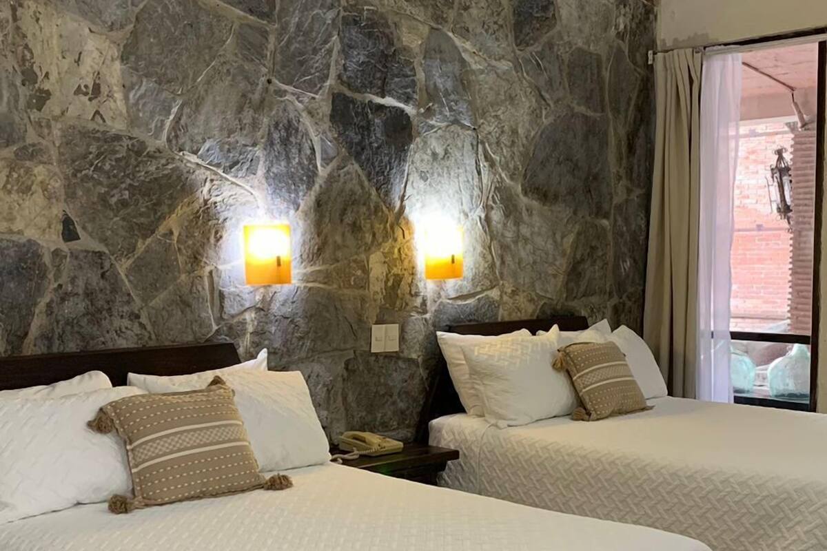 Une chambre d’hôtel avec deux lits, des murs en pierre et une vue sur l’extérieur.