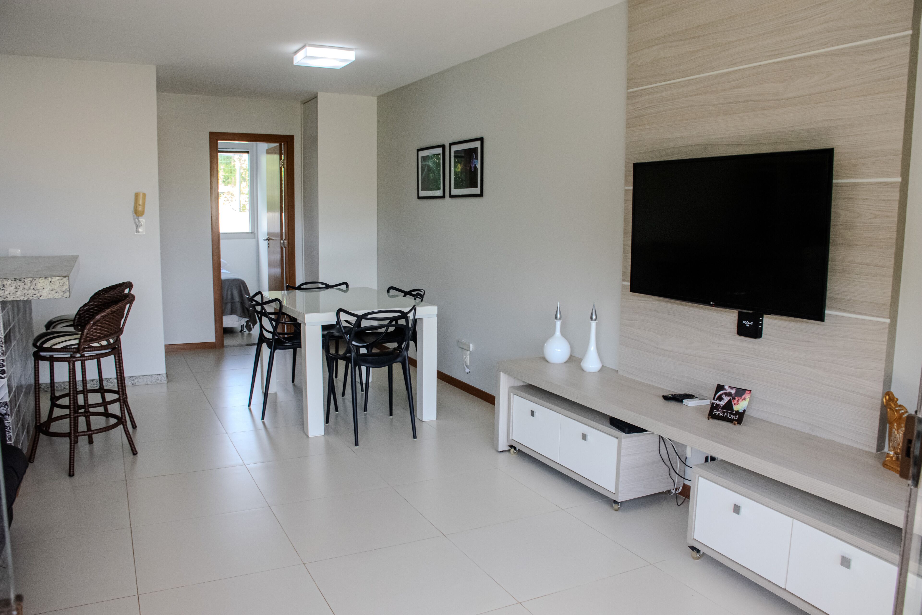 Una sala de estar moderna con un televisor de pantalla plana, una zona de comedor con sillas y una cocina con refrigerador.