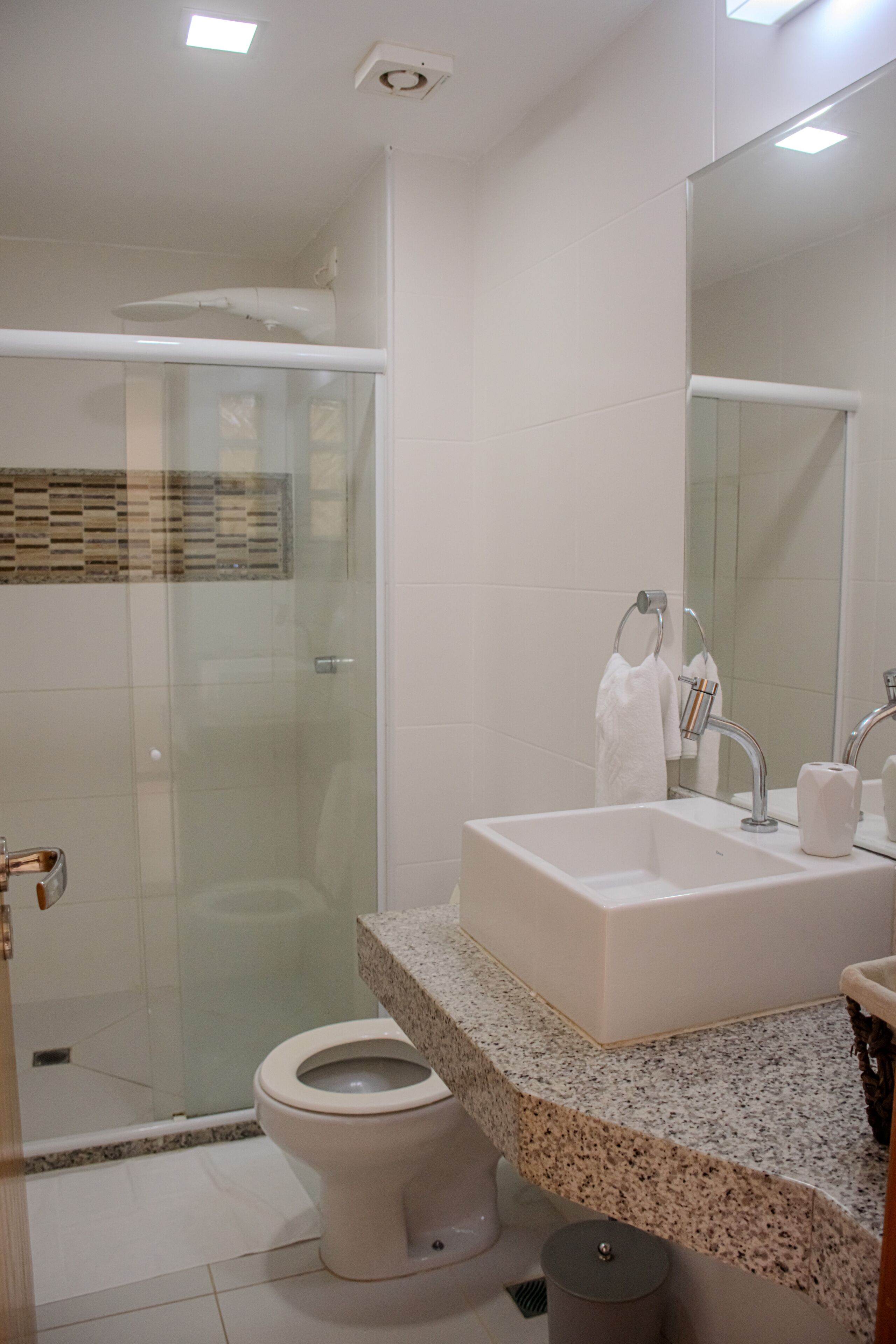 Un baño moderno con cabina de ducha de vidrio, inodoro blanco, lavabo con encimera de granito y espejo sobre el lavabo.