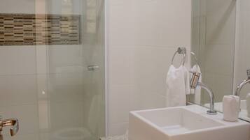 Un baño moderno con cabina de ducha de vidrio, inodoro blanco, lavabo con encimera de granito y espejo sobre el lavabo.