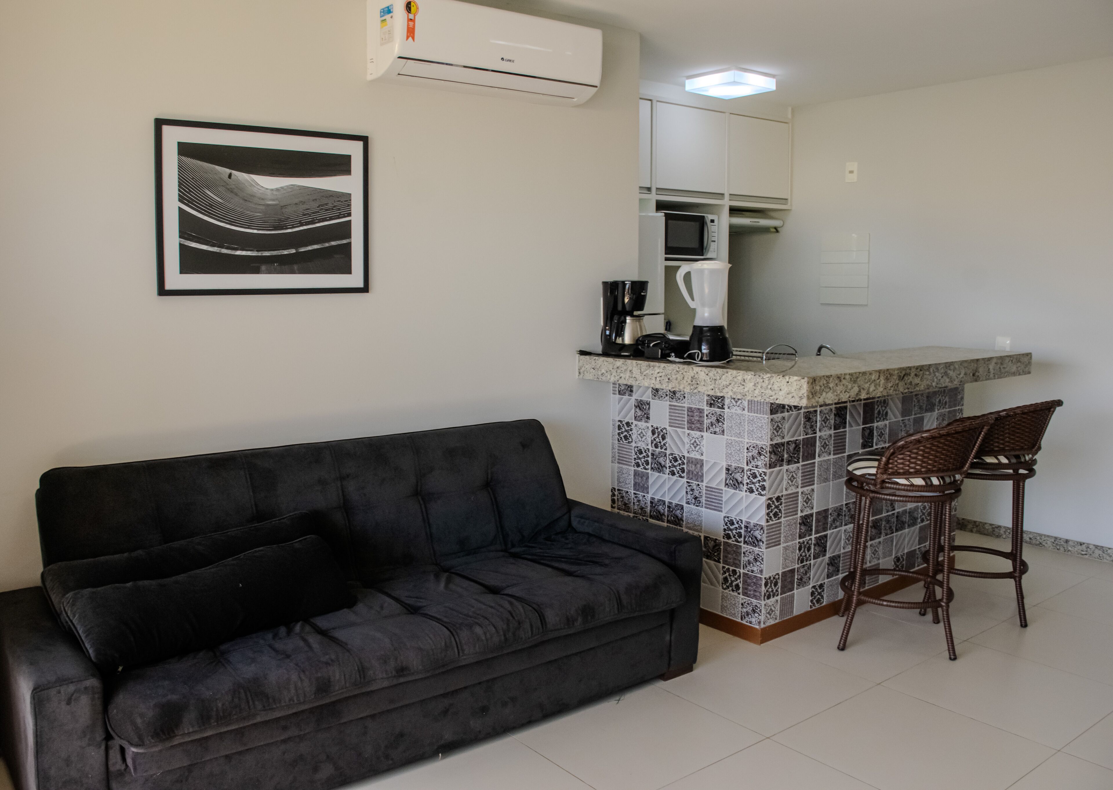 A kitchenette with a microwave, coffee maker, and blender, a black sofa, and a tiled backsplash.