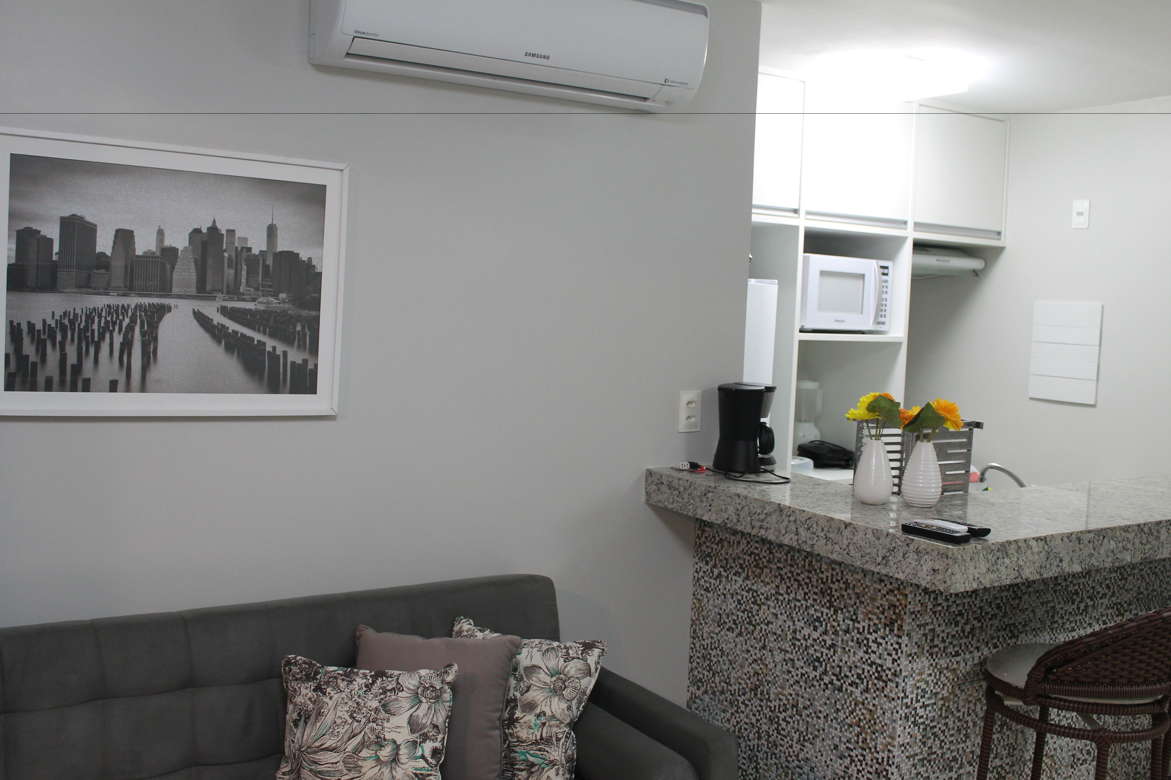 A modern living room with a grey sofa, a coffee machine, and a microwave on a kitchen counter.