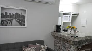 A modern living room with a grey sofa, a coffee machine, and a microwave on a kitchen counter.