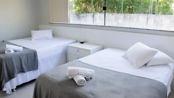 A hotel room with two beds, a small bedside table, and a window with a view of greenery.