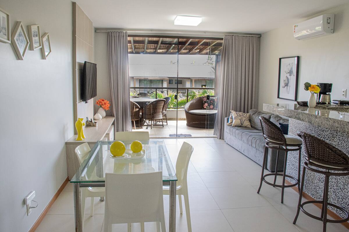 Un salon moderne avec une table à manger en verre, des chaises blanches, un canapé et un coin bar avec des tabourets.