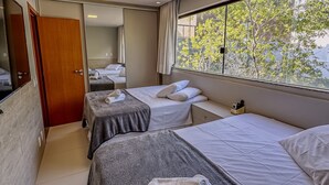 A hotel room with two beds, a large window with a view of trees, a mirror, and a door. - Imbassaí Apartments (Mata de São João)