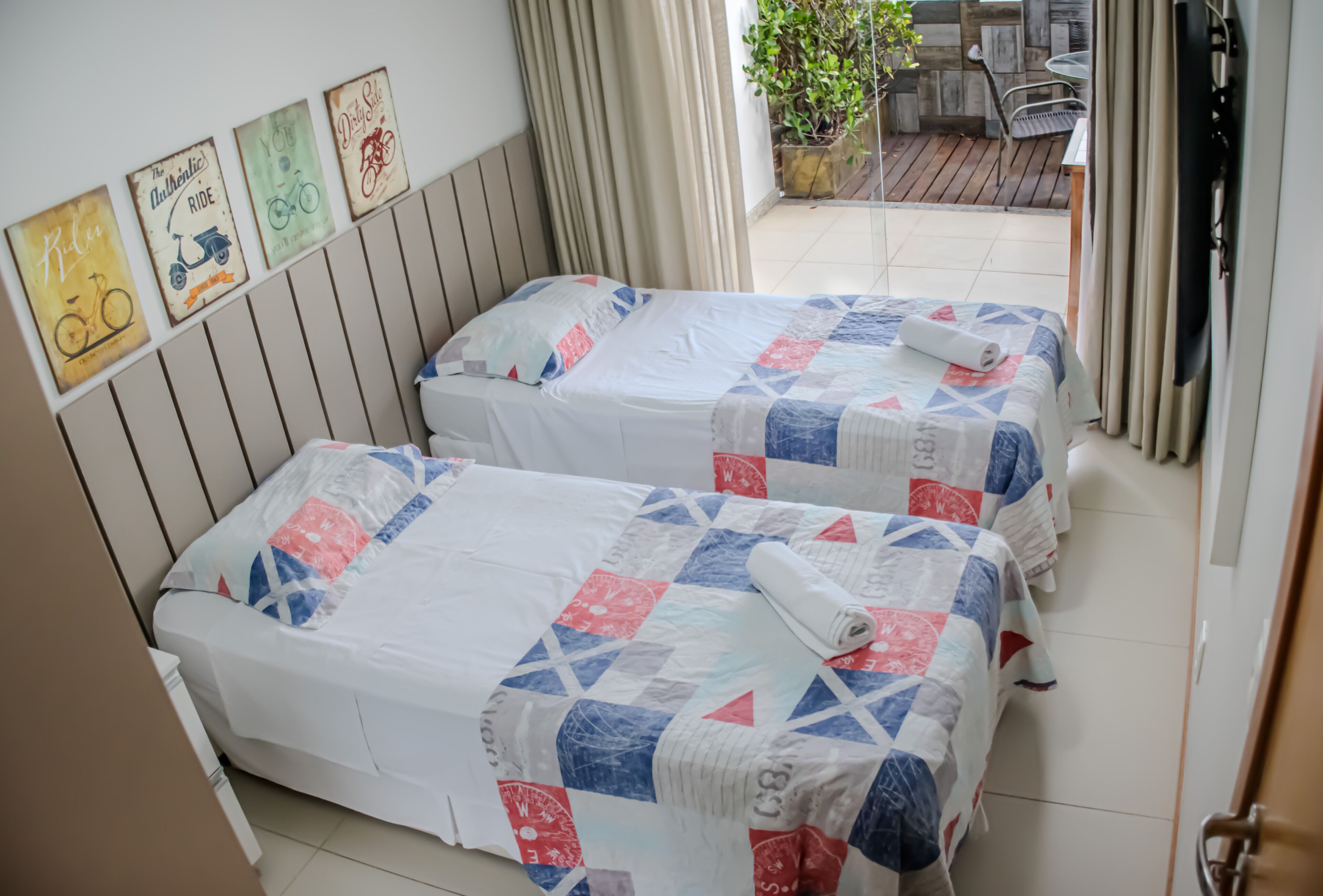 Two beds with matching quilts, a wooden headboard, and a view of an outdoor patio area.