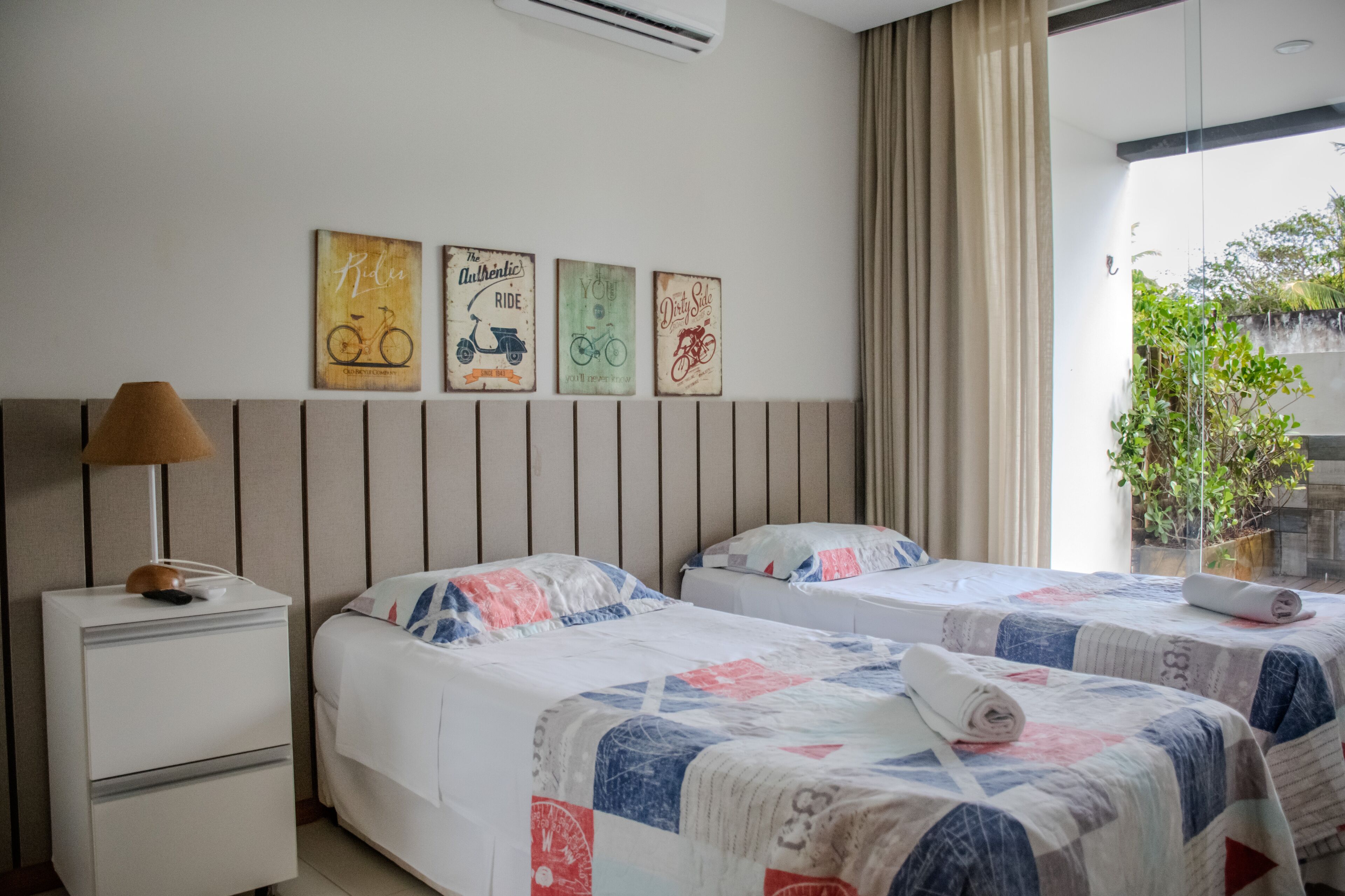 A hotel room with two beds, a bedside table with a lamp, and wall art depicting bicycles.