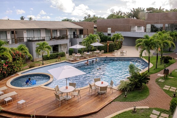 A hotel with a swimming pool, outdoor seating, and lush landscaping. - Imbassaí Apartments (Mata de São João)