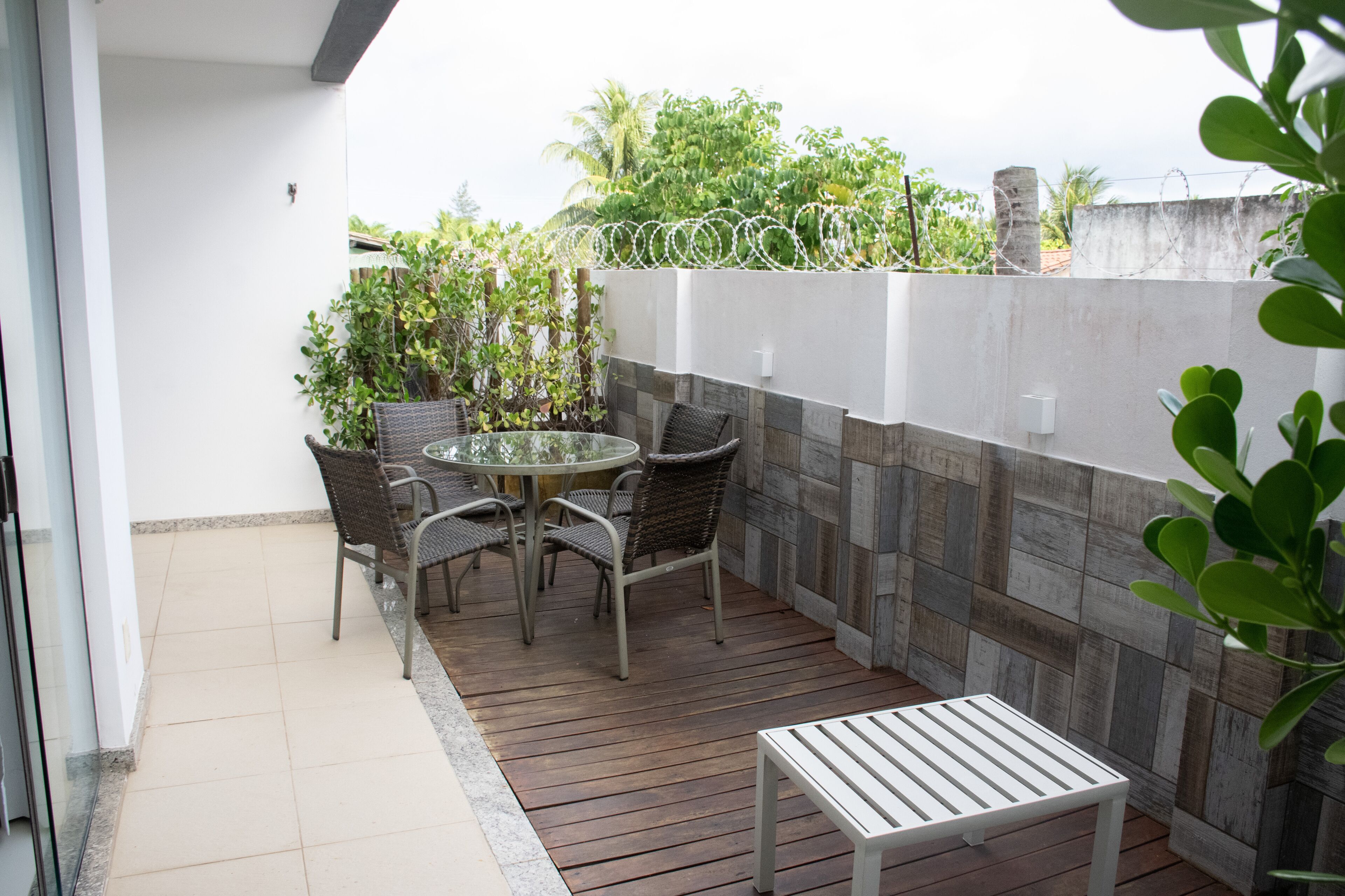 A patio with a round table and chairs, a small white table, and a white wall with a textured pattern.