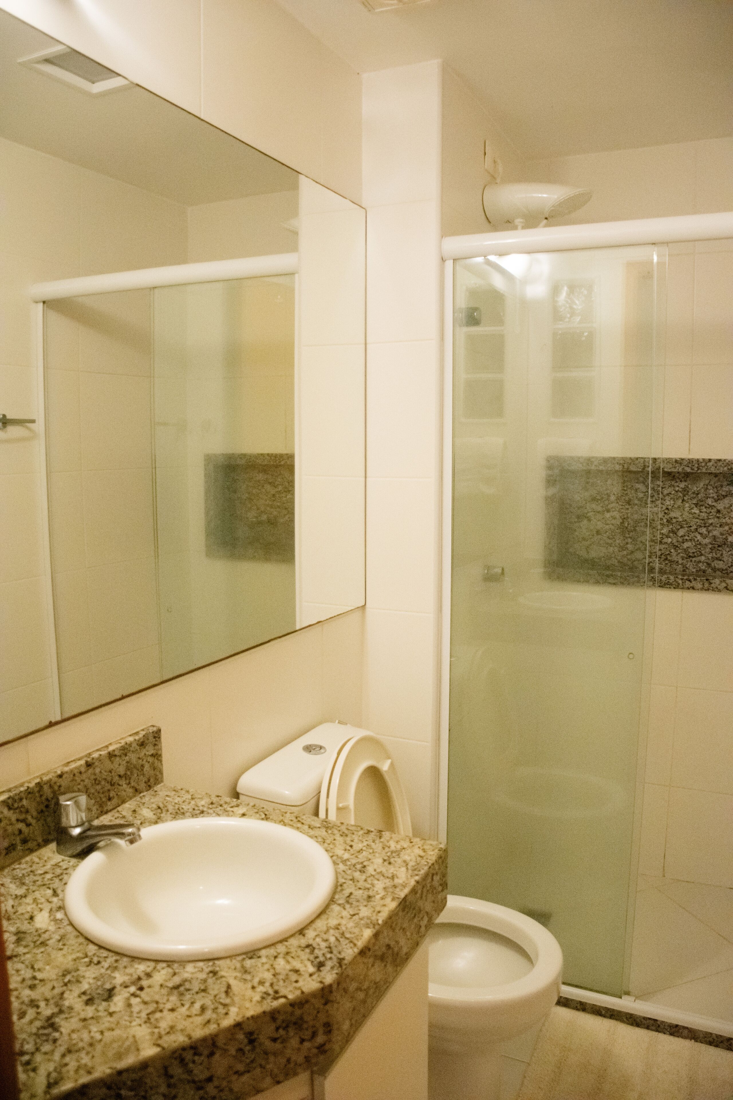 A bathroom with a granite countertop, a white sink, a toilet, and a glass shower enclosure.