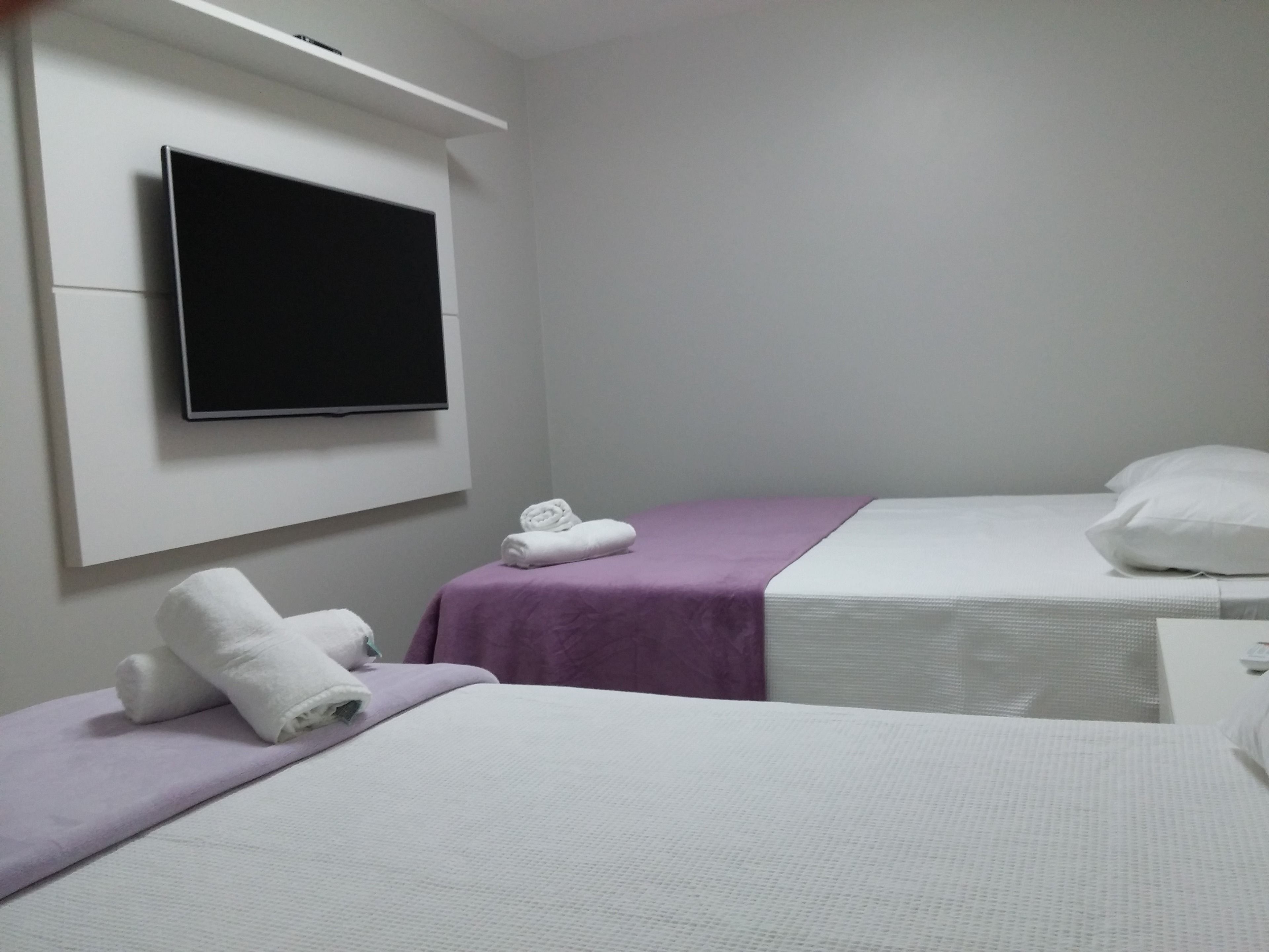 A hotel room with two beds, a TV mounted on the wall, and a small bedside table.