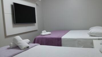 A hotel room with two beds, a TV mounted on the wall, and a small bedside table.