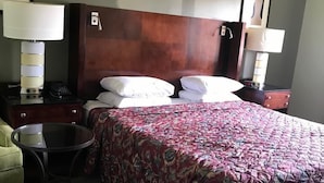 Una habitación de hotel con una cama grande, dos mesitas de noche con lámparas, una pequeña mesa redonda y una silla verde.