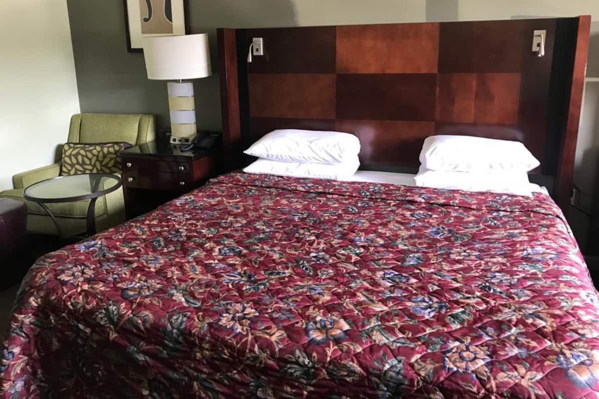 A hotel room with a large bed, a bedside table with a lamp, a chair, and a small round table.