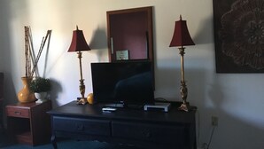 Un mueble bajo de madera oscura con un televisor de pantalla plana, dos lámparas rojas, una planta pequeña y un objeto decorativo en la pared.