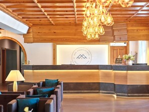 A reception area with a wooden ceiling, a reception desk, and a seating area with sofas. - Erlebnis Hotel Chiemgauer Hof (Inzell)
