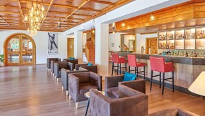Zona de bar con techo de madera y barra con varias botellas. Varias sillas y una escalera que sube a otro nivel.