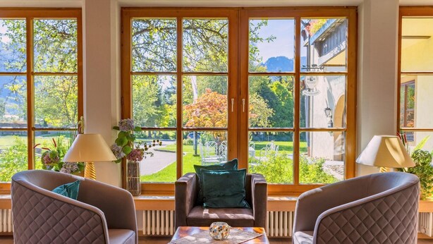 Una habitación con ventanas amplias, dos sillones, una mesita y una lámpara.